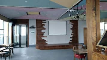 Un salón de conferencias con una pantalla grande, detalles de madera y una lámpara en el techo.