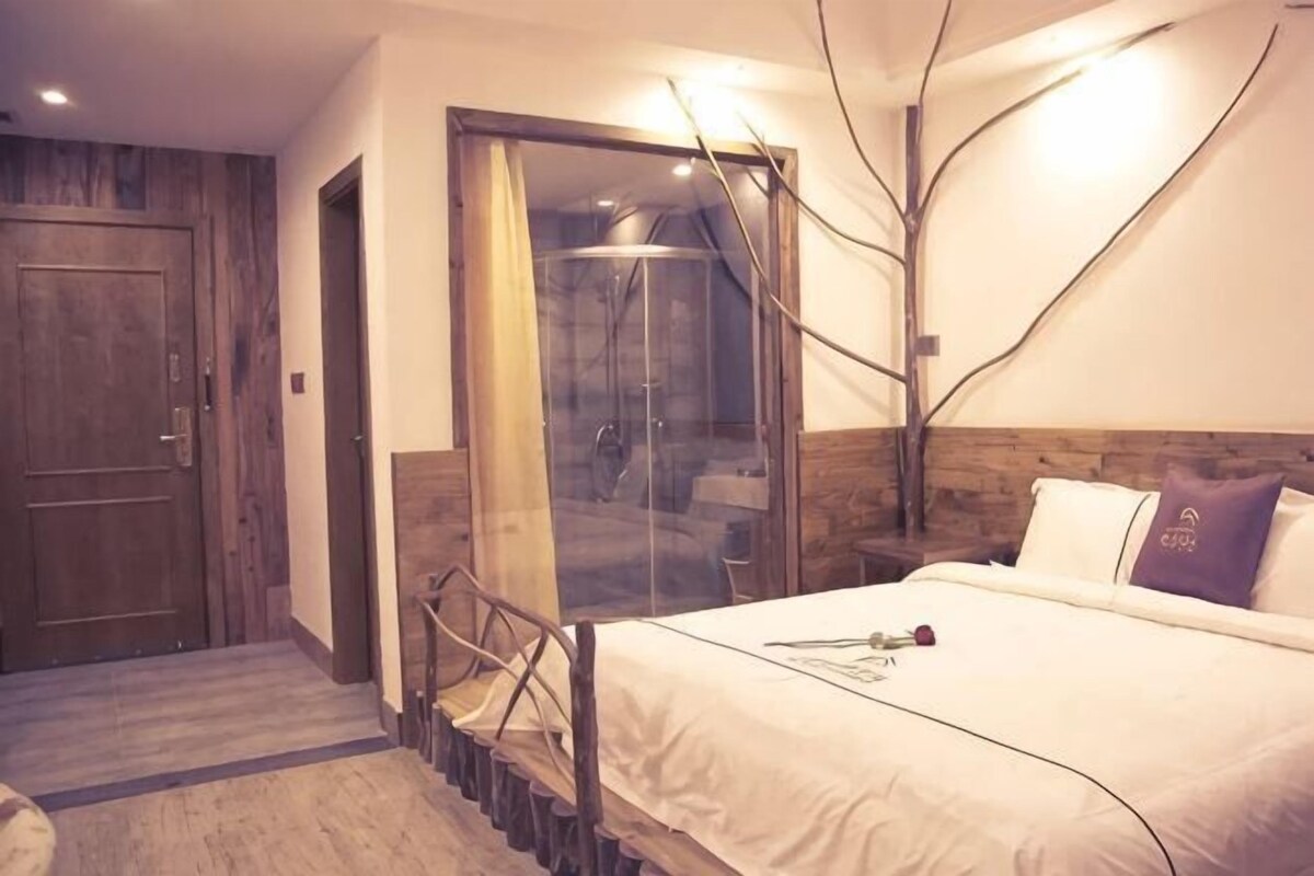 A bedroom with a bed, a wooden door, a glass shower enclosure, and a wooden headboard.