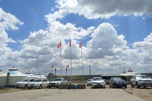 A parking area with several cars and a building with a blue roof. - Ulan tuya hosts tribes in the helamuren steppe (Damao Banner)