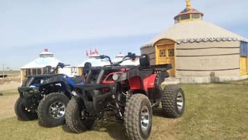 A yurt with a traditional design, a red and black ATV parked in front, and a blue and white vehicle in the background.