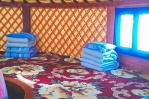 A room with a patterned carpet, a window with blue curtains, and stacks of folded blankets. - Ulan tuya hosts tribes in the helamuren steppe (Damao Banner)