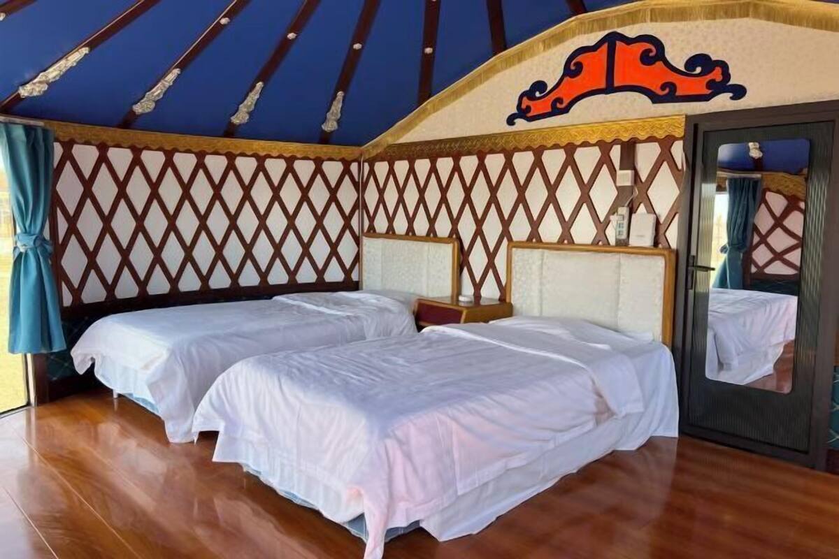 A room with two beds, a wooden floor, and a decorative ceiling.