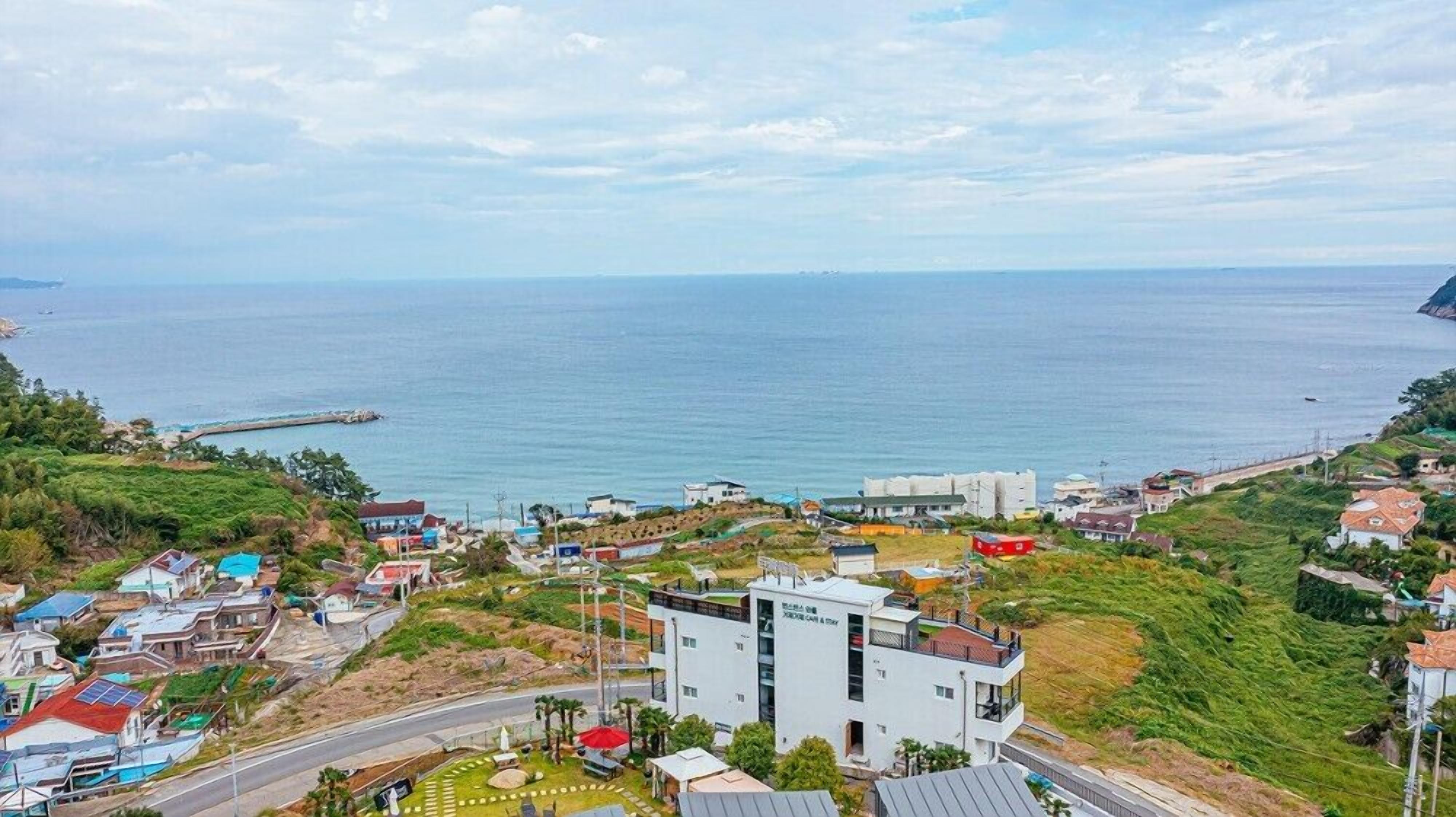 Un pueblo costero con una mezcla de edificios residenciales y comerciales, un edificio blanco destacado con señalización, y una vista despejada del mar.