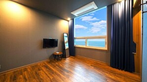 A room with a large window, wooden flooring, a flat-screen TV, and a small table. - Geoje Beans Pension (Geoje)