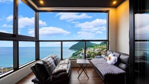 A modern living room with a large window offering a scenic view of the sea and a mountainous landscape. - Geoje Beans Pension (Geoje)