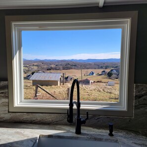 Casa de banho com janela que oferece vista para uma paisagem rural, incluindo campos e montanhas ao longe.