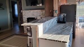 A modern kitchen with a stone backsplash, wooden cabinets, a built-in TV, and a refrigerator. - Thomas Cottage at Angel Acres (Fincastle)