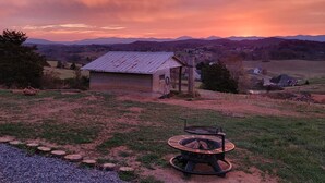 A rustic cabin with a metal roof, surrounded by a gravel path and a fire pit. - Thomas Cottage at Angel Acres (Fincastle)