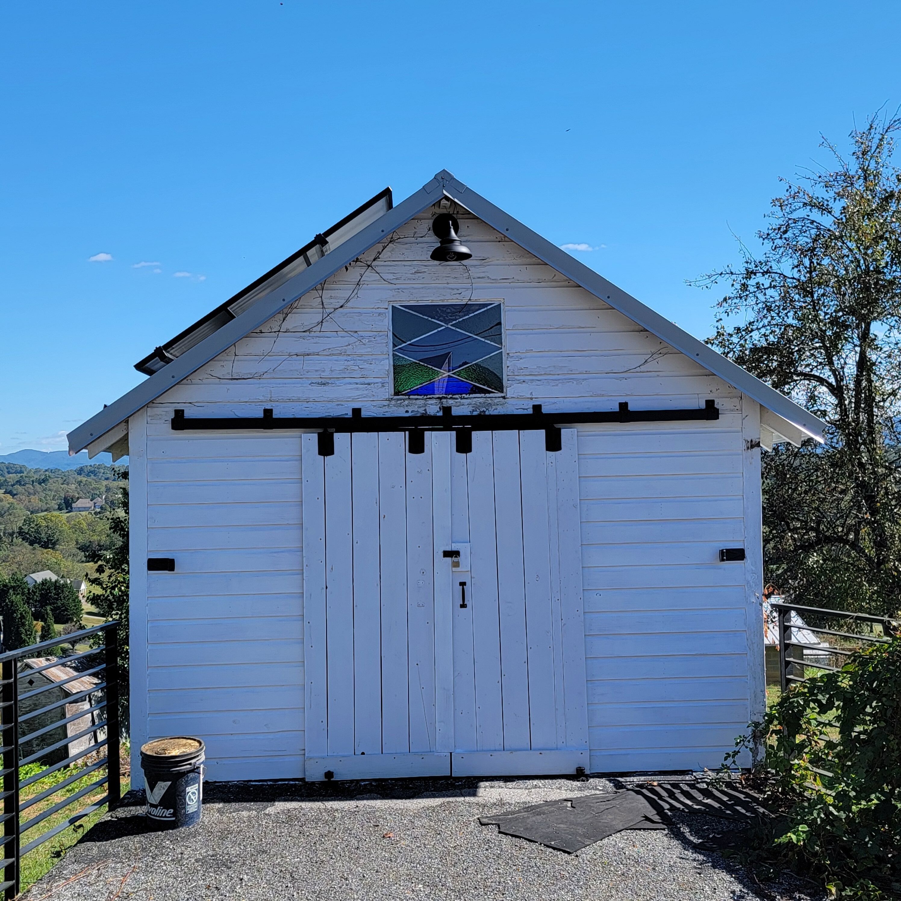 A white barn with a triangular roof and a stained glass window.
