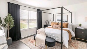 Un dormitorio moderno con cama con dosel, un ventanal con cortinas, una mesita de noche con lámpara y una planta en maceta.