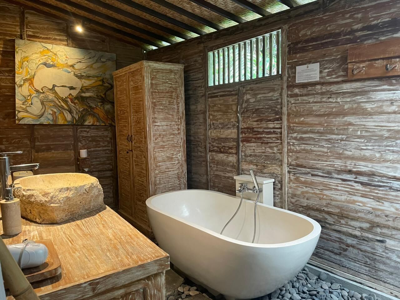 Un bagno moderno con una vasca da bagno indipendente, un lavabo in pietra e un mobile contenitore in legno.