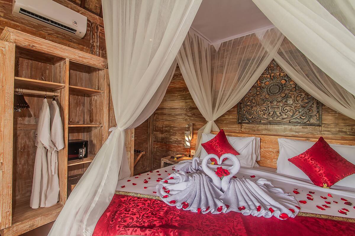 A bedroom with a wooden wardrobe, a bed with red and white bedding, and a decorative wall piece.