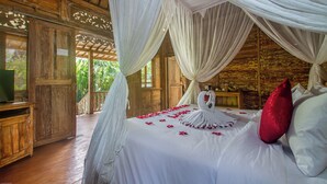 A bedroom with a canopy bed, wooden walls, and a view of greenery outside.