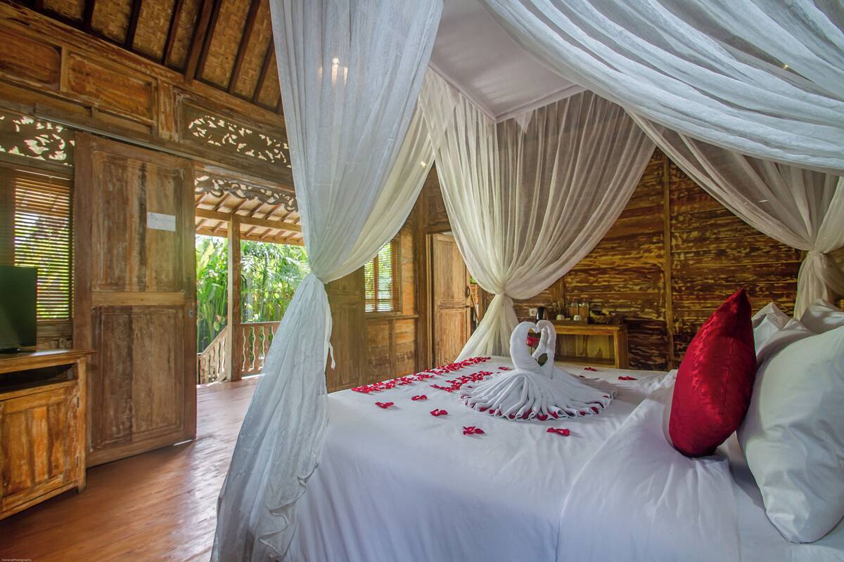 A bedroom with a canopy bed, wooden walls, and a view of greenery outside.