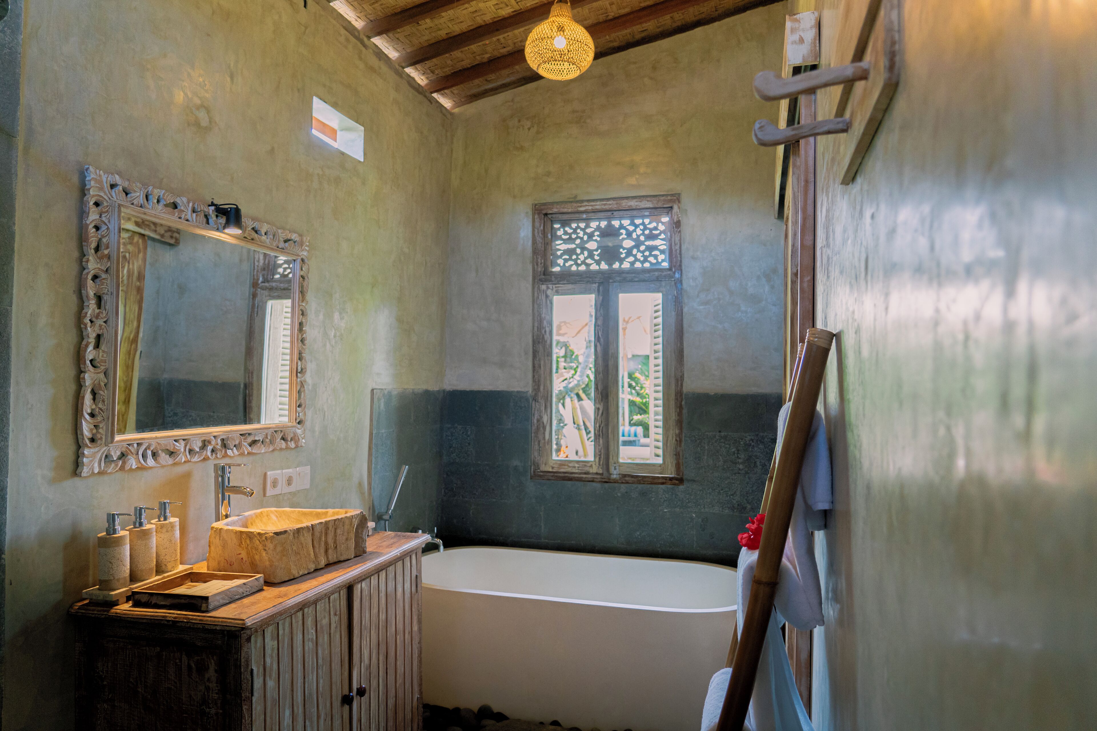 Un baño con un espejo grande, un tocador de madera, una bañera y una ventana con celosía decorativa.