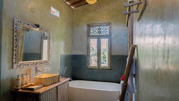 A bathroom with a large mirror, a wooden vanity, a bathtub, and a window with decorative lattice.