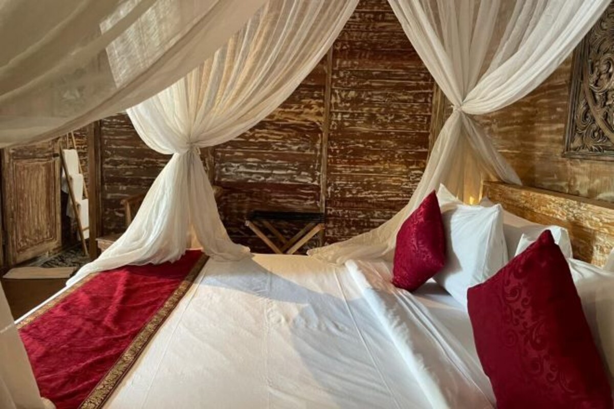 Cama com lençóis brancos, almofadas vermelhas e um dossel.