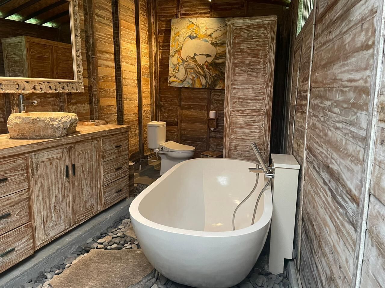 Un baño rústico con una bañera independiente, muebles de madera y un espejo grande.
