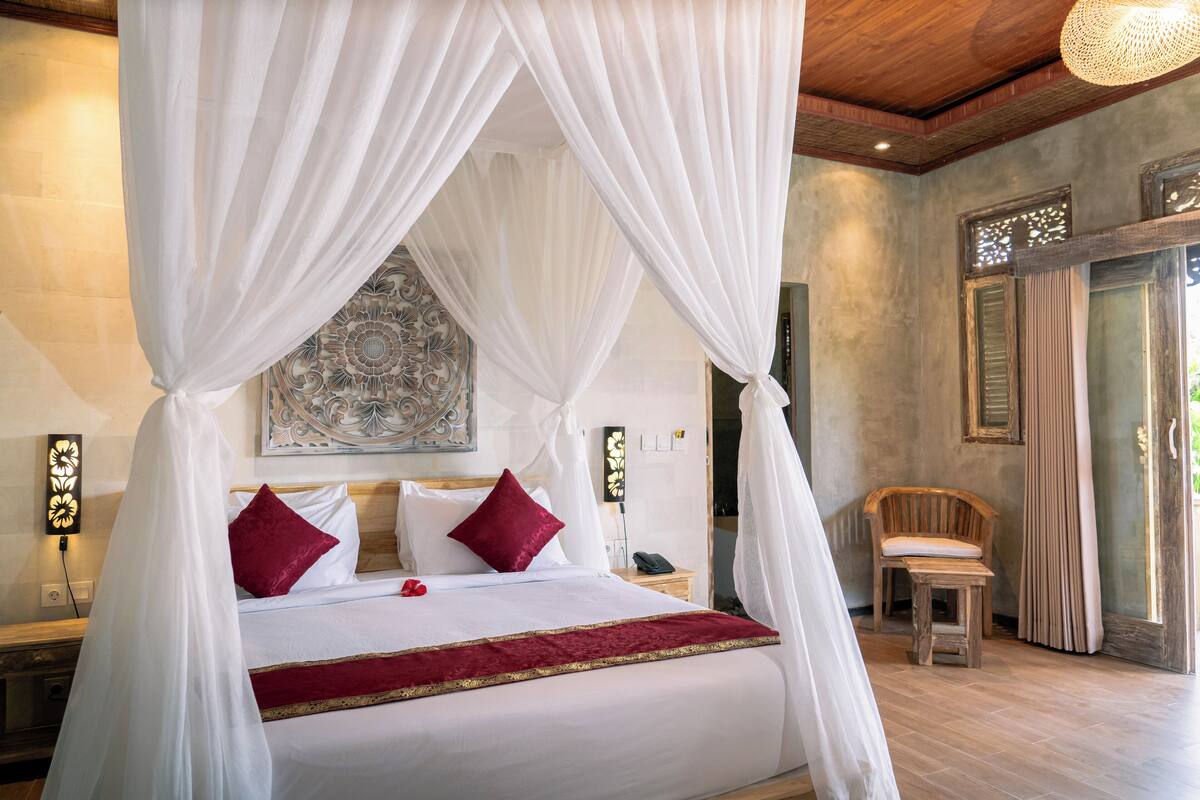 A bedroom with a four-poster bed, a bedside table with a lamp, and a chair.