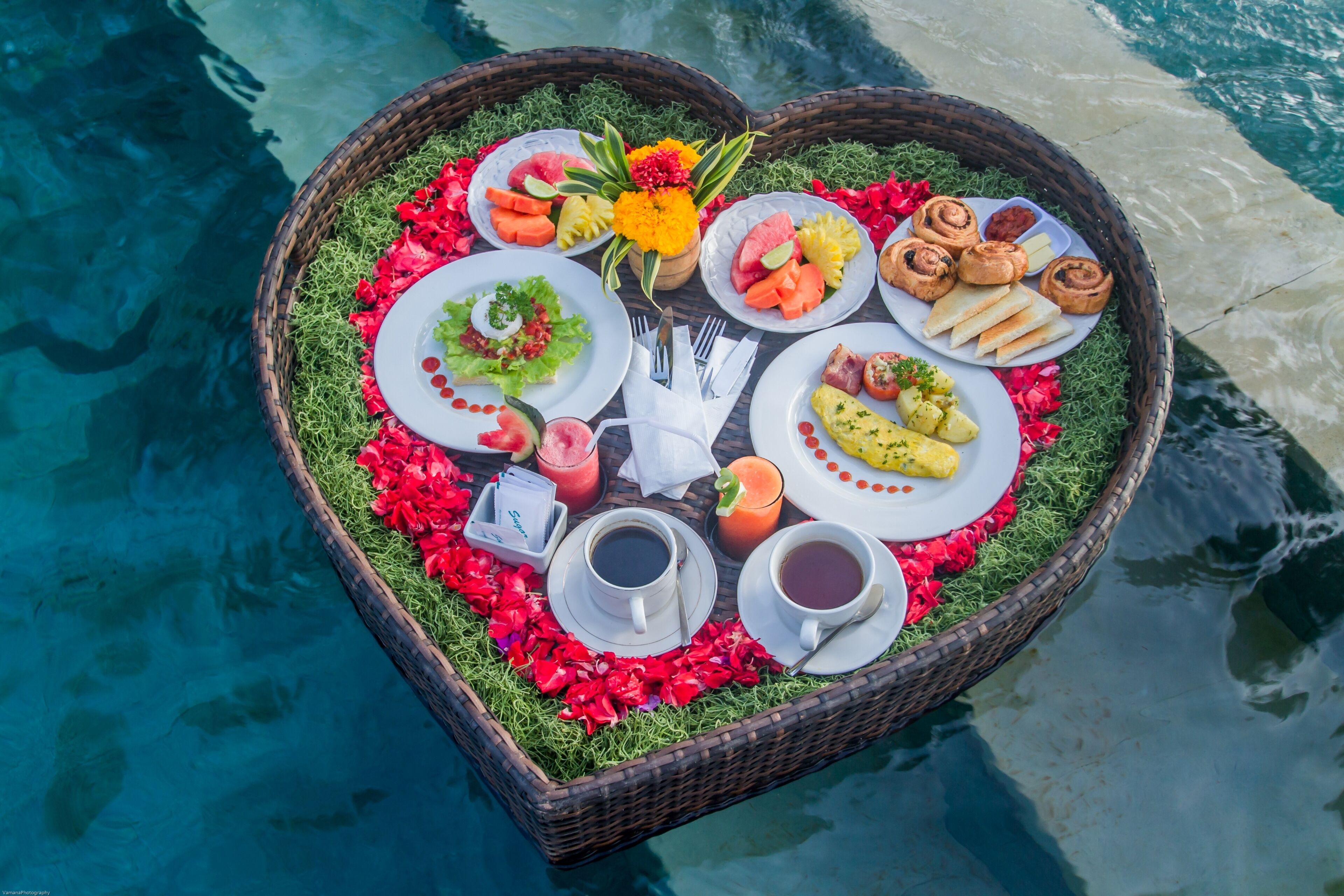 Bandeja em formato de coração com comida e bebidas ao lado de uma piscina.
