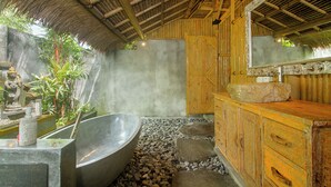 A bathroom with a large freestanding bathtub, a wooden vanity with a stone sink, and a mirror.