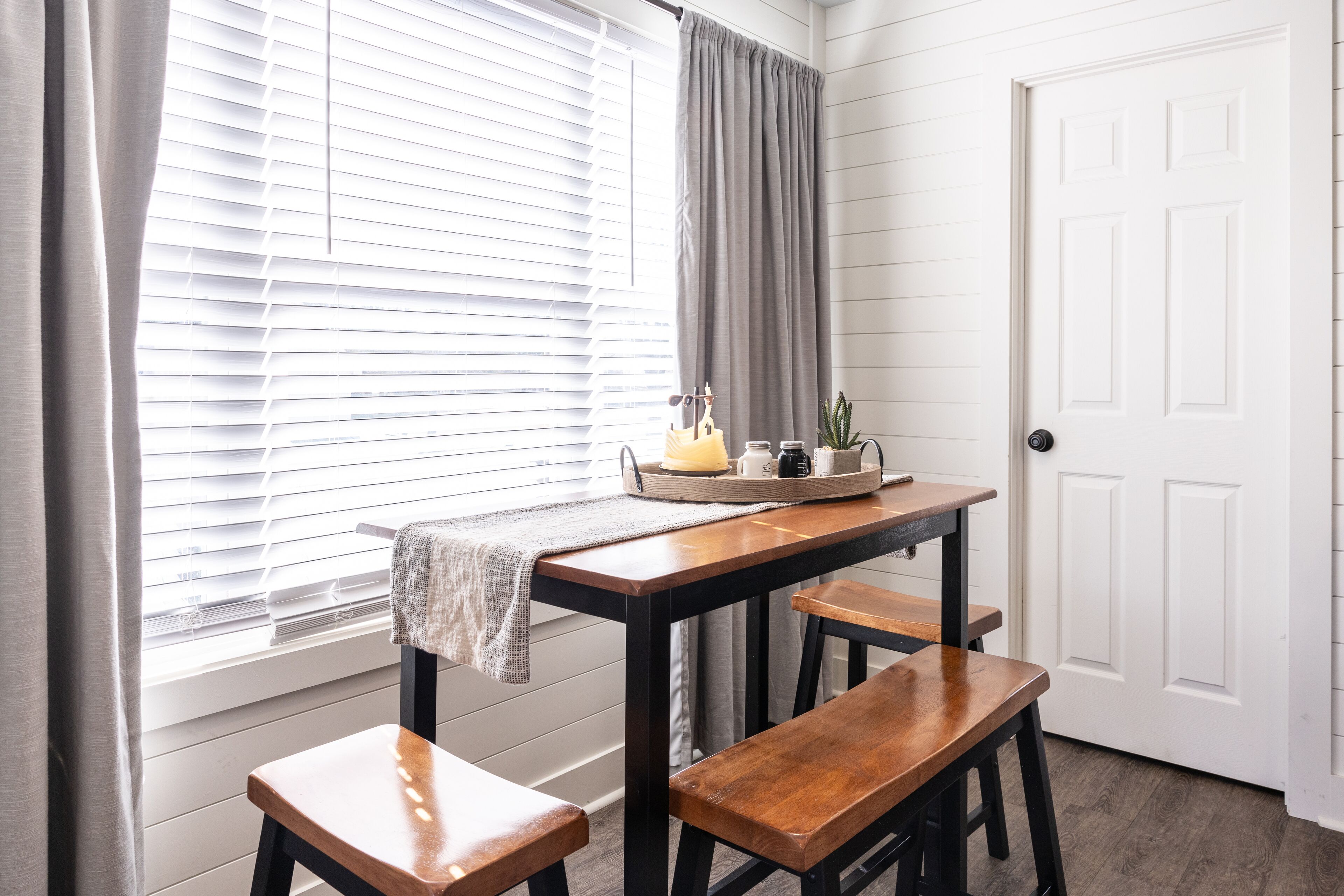 A dining area with a wooden table and benches, a window with blinds, and a door.