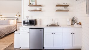 Una cocina moderna con armarios blancos, un microondas integrado y un lavavajillas. Encima de la encimera hay estantes de madera con frascos y un cuadro enmarcado.