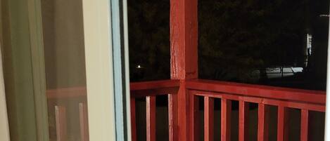 A balcony with a red railing, a glass door with a black handle, and a dark night sky in the background.
