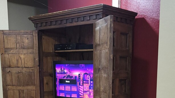 Ein Holzunterhaltungsschrank mit Fernseher, einer roten Wand und einem Fliesenboden.