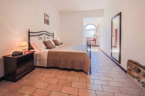 A bedroom with a bed, bedside table, lamp, and a view of a balcony.