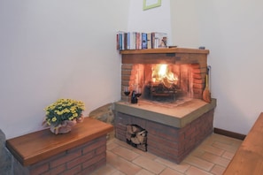 A fireplace with books on the mantel, a vase of flowers, and a log storage area. - Villa Fornace by MMega (Lisciano Niccone)