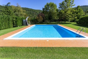 A rectangular swimming pool with a clear blue water surface, surrounded by a brick deck and a grassy lawn. - Villa Fornace by MMega (Lisciano Niccone)