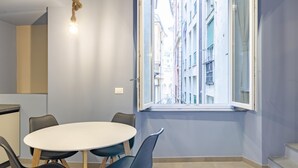 A modern room with a round table, chairs, a hanging light fixture, and a large window with a view of buildings. - San Luca Apartments - Fieschi by Wonderful Italy (Genoa)