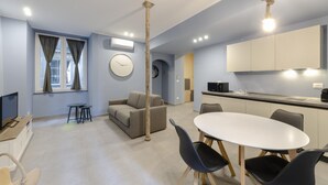A modern living room with a sofa, a dining table with chairs, a TV, and a kitchen area with cabinets and a microwave. - San Luca Apartments - Fieschi by Wonderful Italy (Genoa)