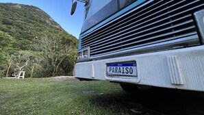 A bus with a license plate reading "PARAISO" parked on a grassy area with a mountainous backdrop. - House on a BUS by the river (Florianópolis)