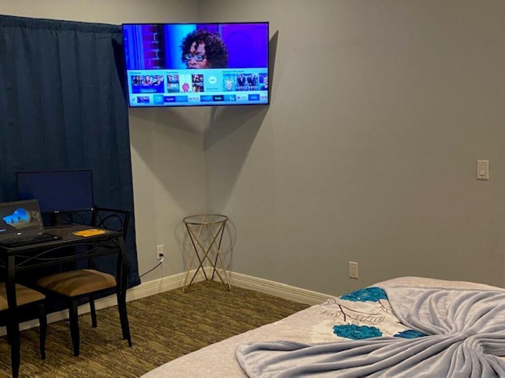 Una stanza con un letto, una scrivania con un portatile, una TV fissata al muro e un tavolino.