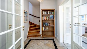 Un pasillo con una escalera de madera, una estantería y una puerta que da a otra habitación.