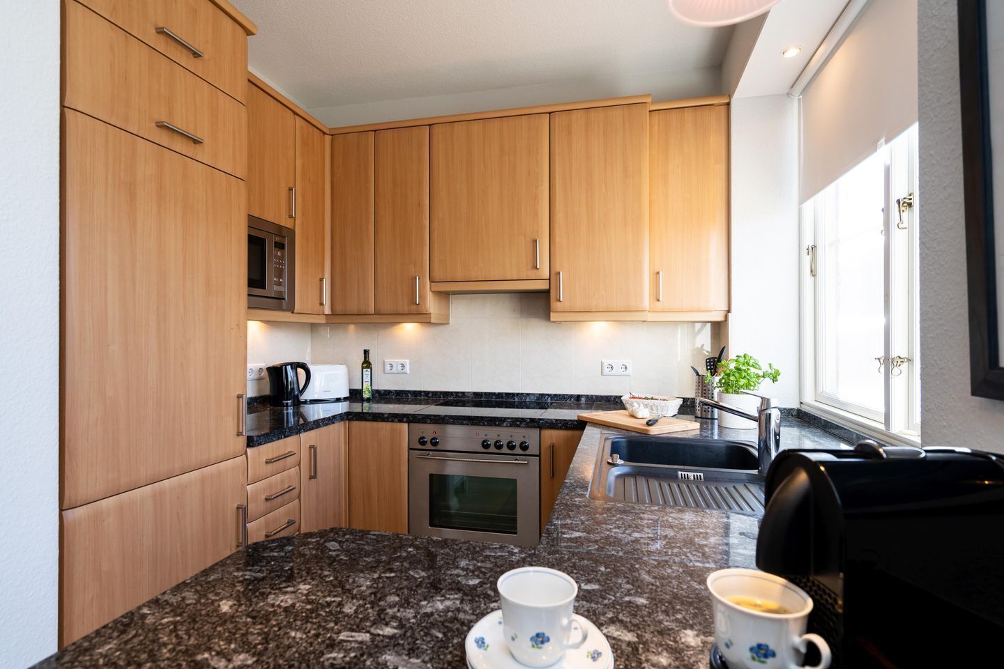 Eine moderne Küche mit Holzausstattung, einer Granit Arbeitsplatte, einer Mikrowelle, einem Backofen und einem Spülbecken.