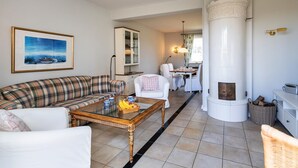 Una sala de estar con un sofá, una mesa de centro con frutas, una chimenea y un comedor con sillas y una mesa.