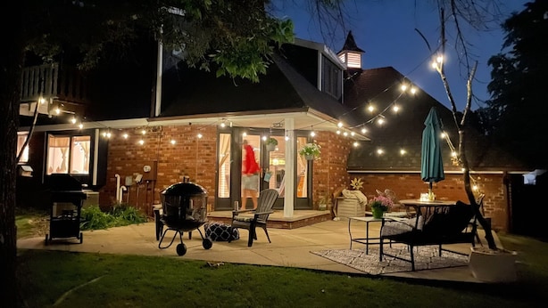 Une terrasse à l’arrière de la maison, équipée d’un barbecue, de meubles d’extérieur et de guirlandes lumineuses.