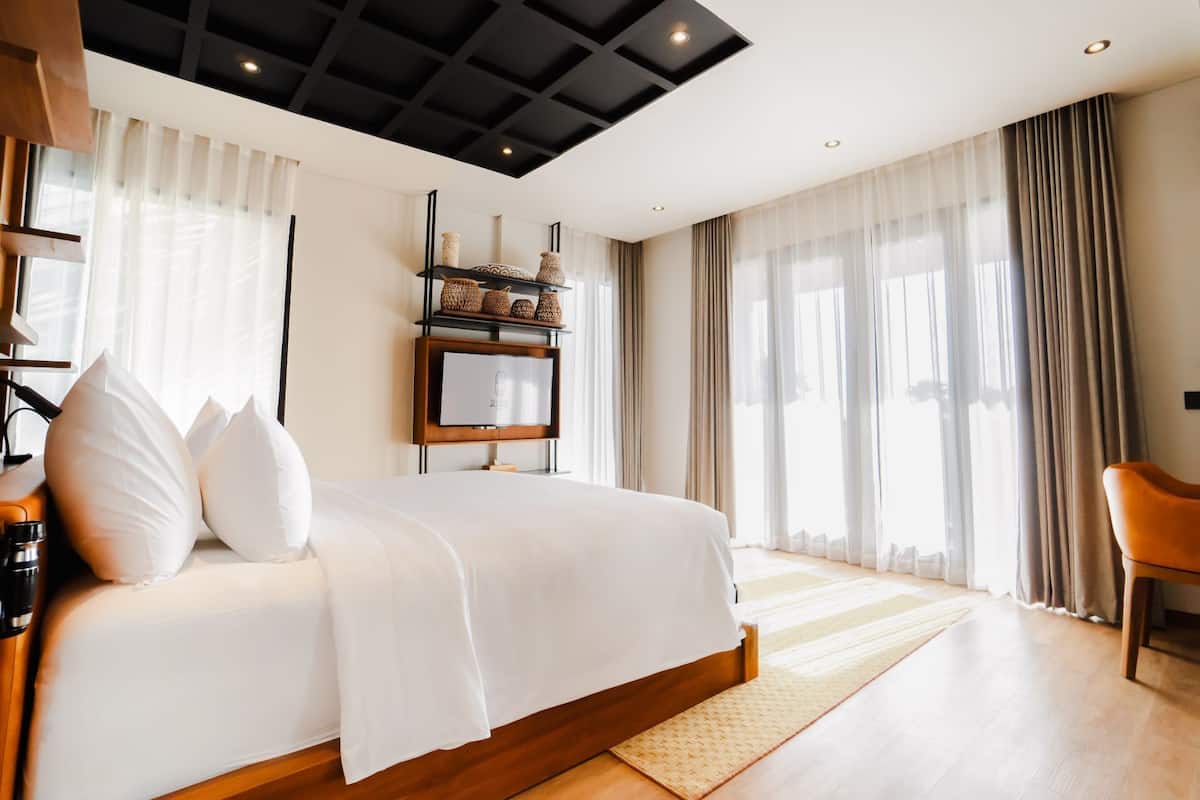 Un dormitorio moderno con una cama grande, una mesita de noche de madera, un televisor de pantalla plana y una estantería con objetos decorativos.