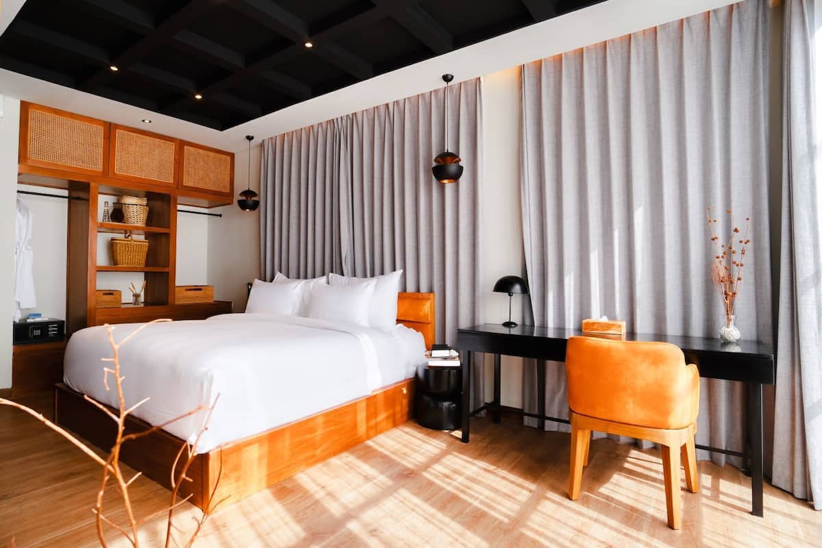 Un dormitorio moderno con una cama de madera, un escritorio y una silla. Se aprecia un armario con estantes y un cesto colgado.