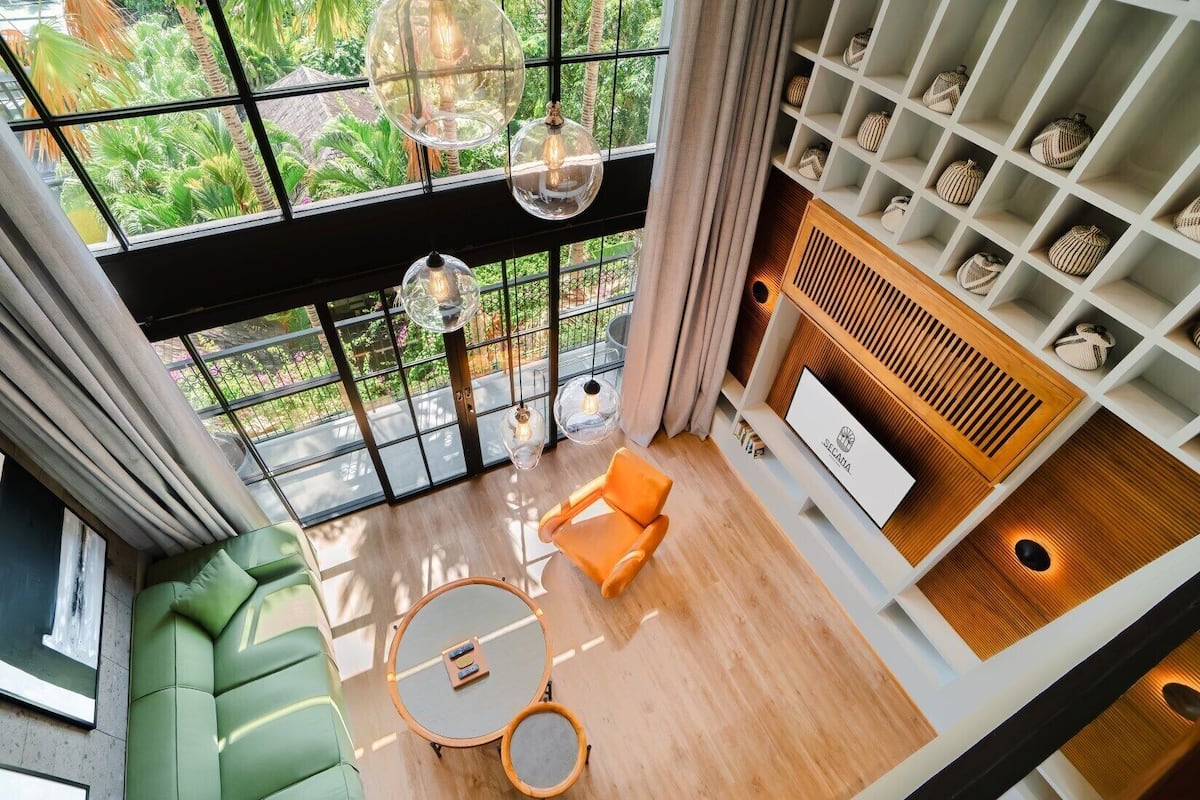 Una sala de estar moderna con un sofá verde, un sillón naranja y una mesa de centro redonda. Hay lámparas colgantes y una chimenea con adornos decorativos.