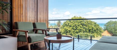 A wooden deck with a view of the ocean, a green chair, a round table, and a sofa.