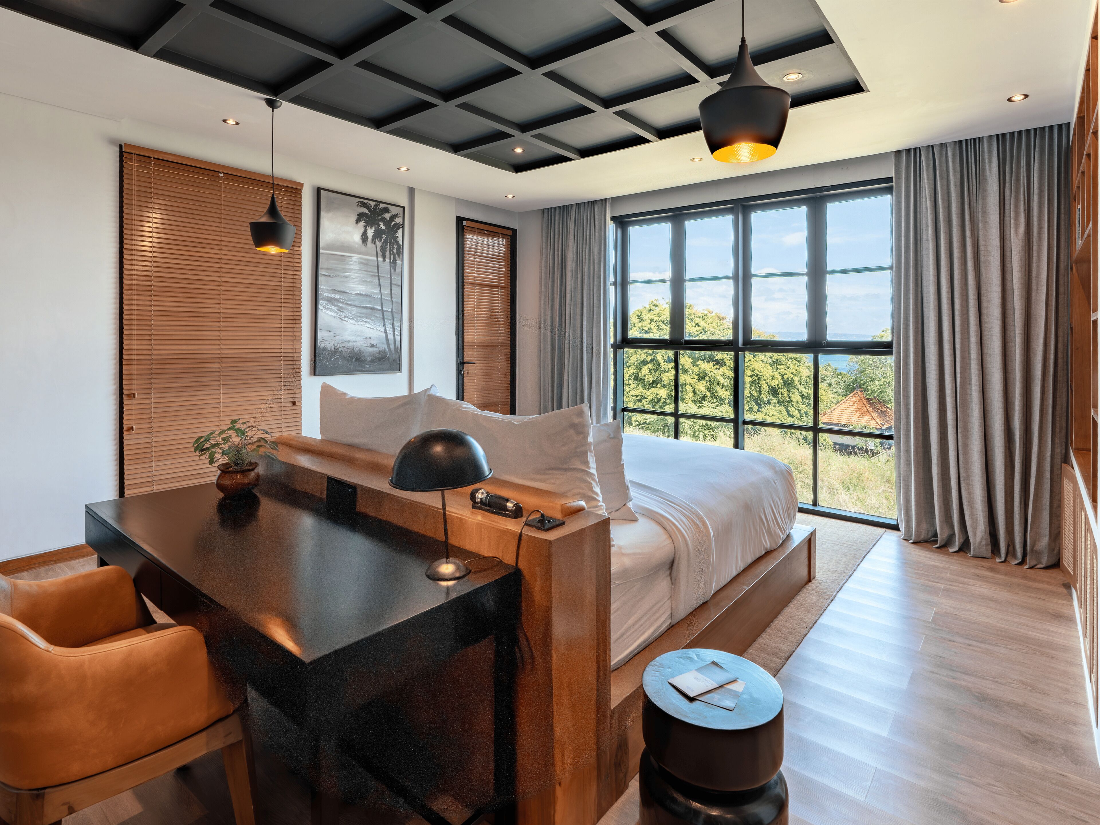 A modern hotel room with a large bed, a desk, a chair, a round side table, and a view of the outdoors.