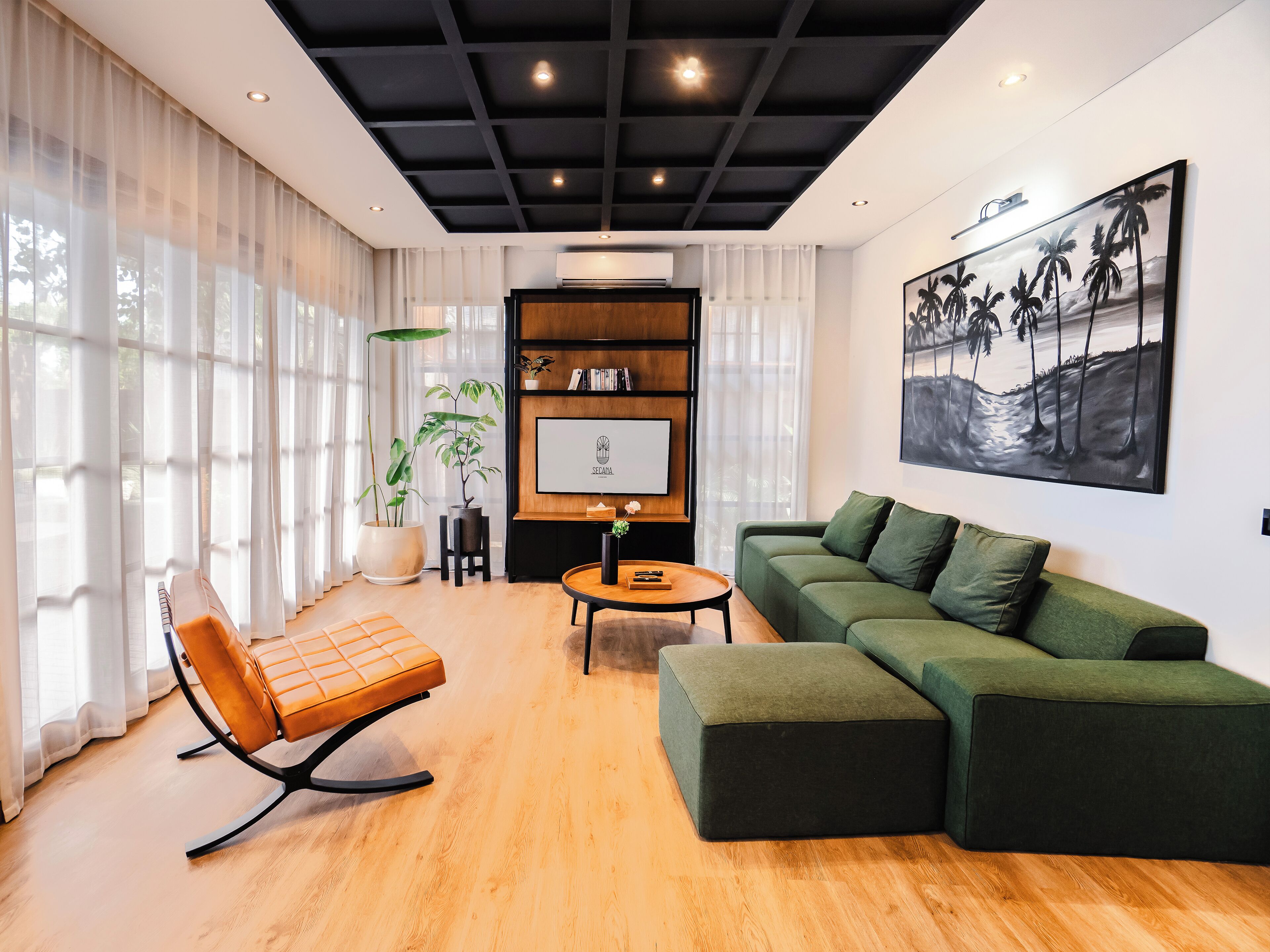 Un soggiorno moderno con un divano verde, un tavolino in legno e una poltrona in pelle. Si nota una libreria con libri e un quadro incorniciato appeso al muro.