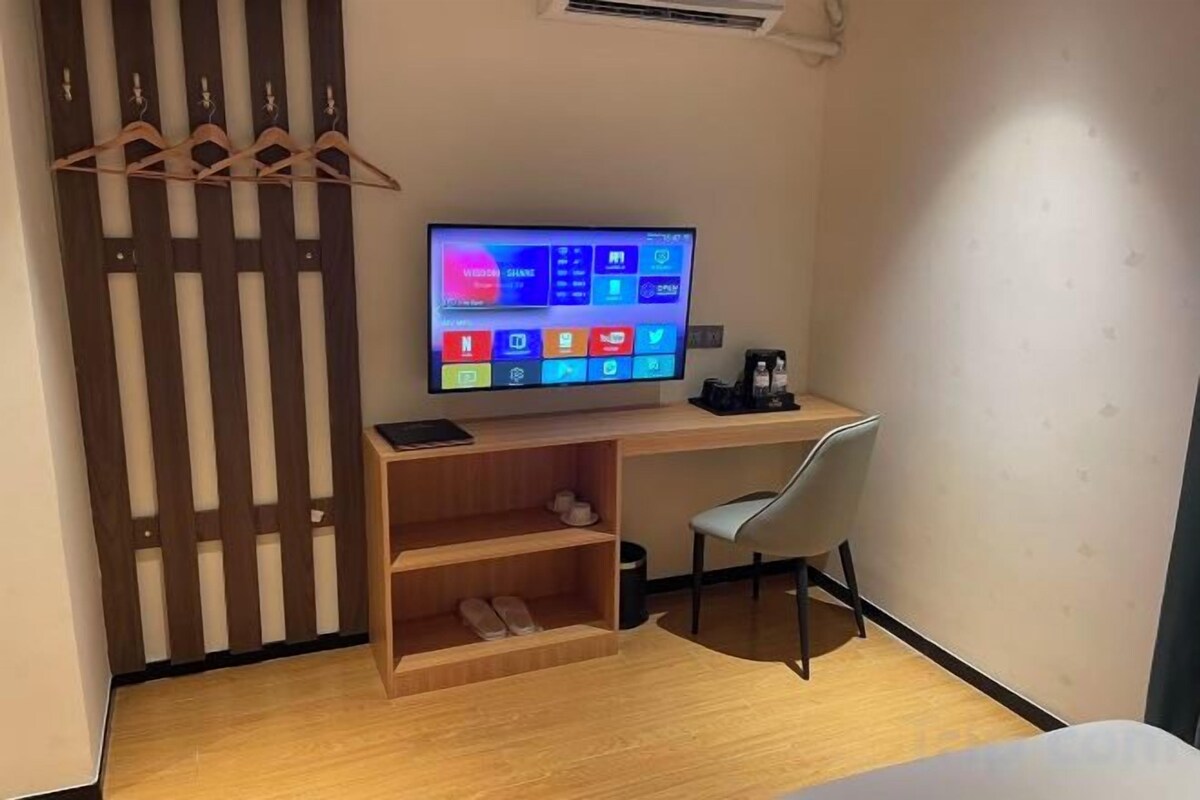 A room with a desk, a chair, a television, and a wooden shelf.