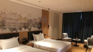 A hotel room with two beds, a large wall mural, a seating area with a table, and a view of the mountains. - Jinjiang Star Hotel (Pasay)