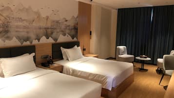 A hotel room with two beds, a large wall mural, a seating area with a table, and a view of the mountains.