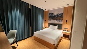 A hotel room with a large bed, a desk, a chair, a nightstand with a phone, and a wall with a mountain painting. - Jinjiang Star Hotel (Pasay)